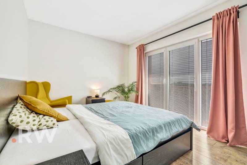 A bedroom with a yellow armchair, a bed, and pink curtains in a three-room apartment.