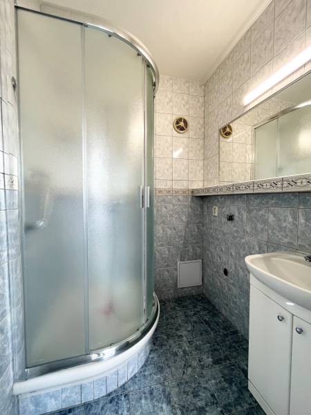 Bathroom in a 2-room apartment with a corner shower and a sink with storage space.