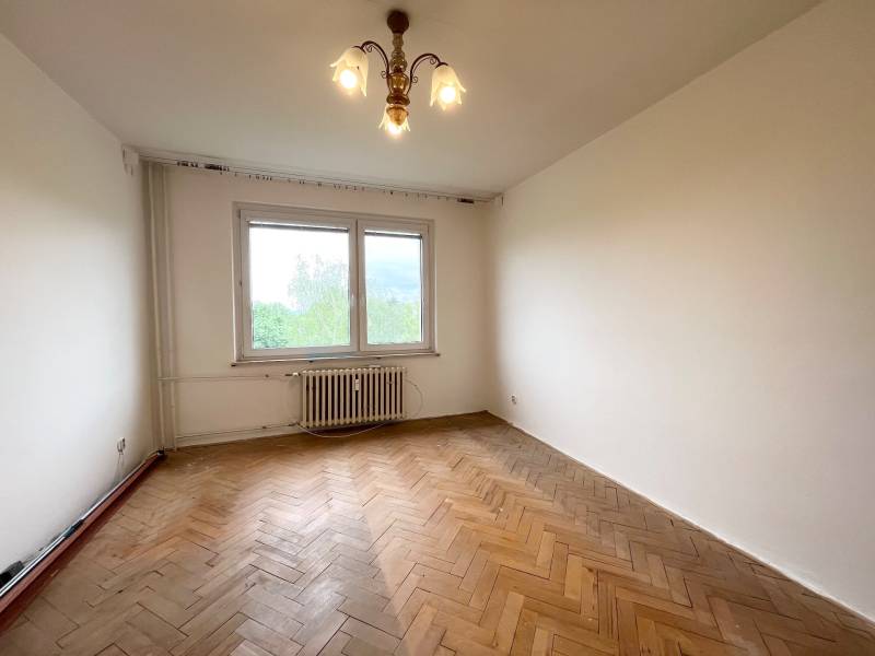 An empty room with parquet flooring and a large window in a 2-room apartment.