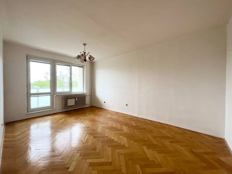 A spacious room with wooden flooring and a large window in a 2-room apartment.