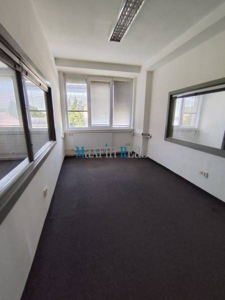 A narrow office with windows and carpet, white walls, suitable for a workspace.