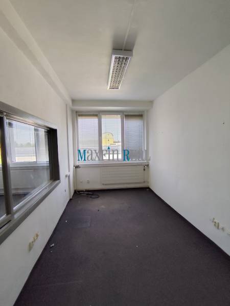 An empty office space with a window and radiator, ready for rent.