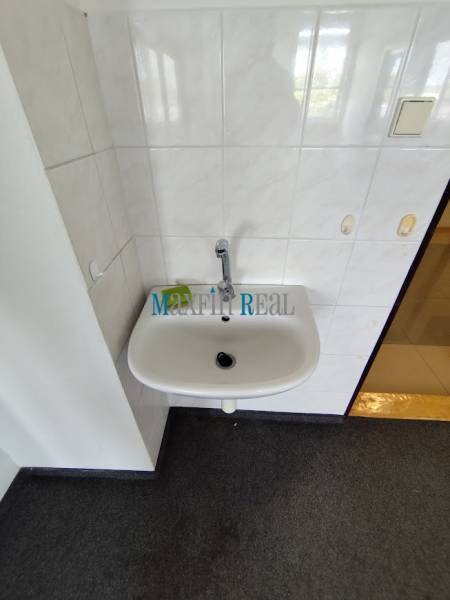 A sink in the office bathroom with white tiles and a dark carpet.