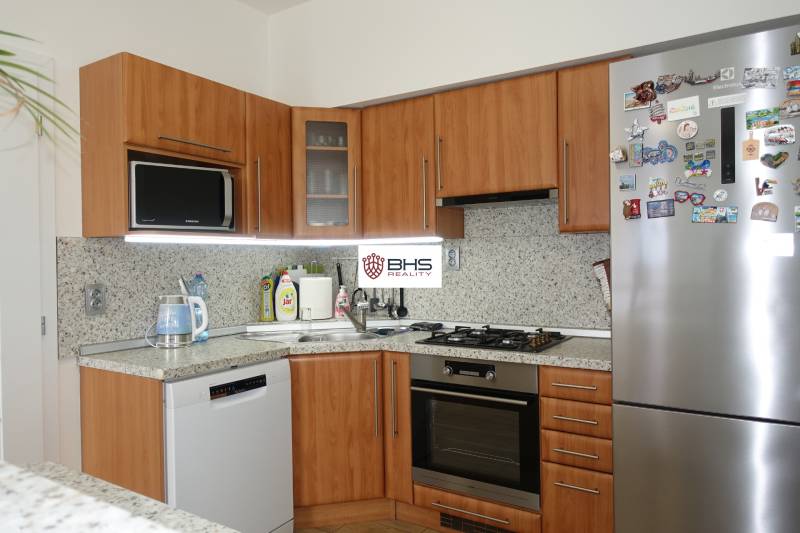 A kitchen in a 3-room apartment with wooden cabinets and stainless steel appliances.