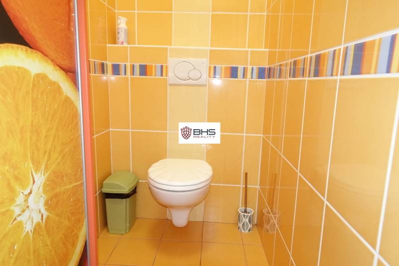 A toilet in a 3-room apartment with orange-yellow tiles and orange decoration.