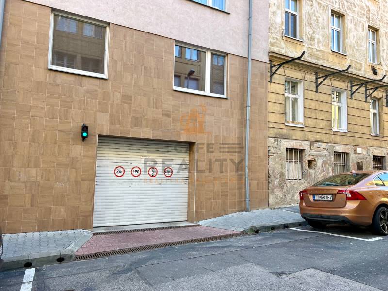 A gate in the city center with traffic signs and a brown car, garages in the background.