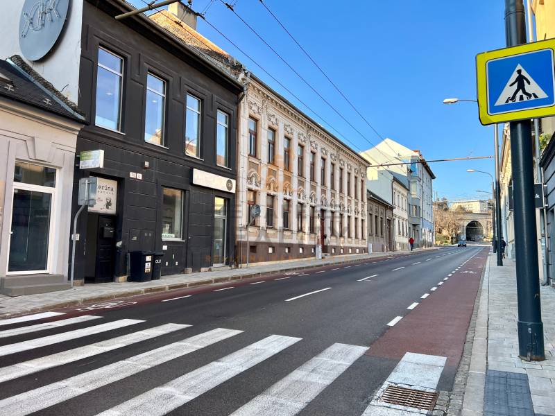 A street with a crosswalk, historic buildings, and a blue sky. Traffic signs, a bicycle path, and garages.