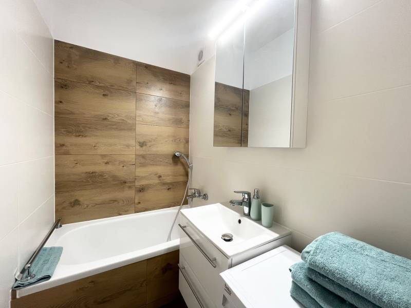 A bathroom in a studio apartment with a bathtub, a mirrored cabinet, and light blue towels.