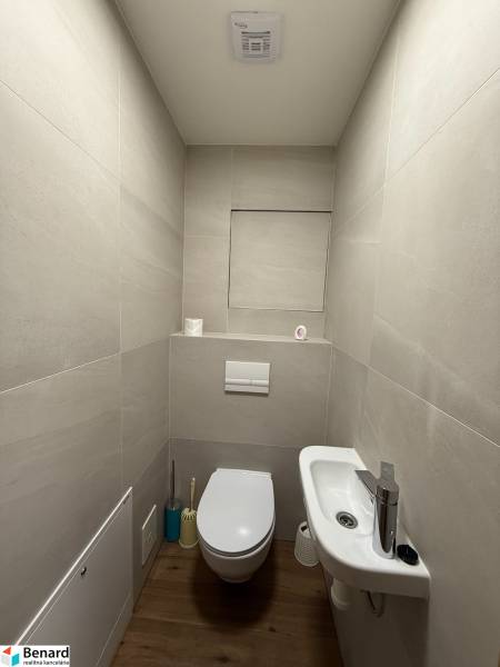 Bathroom with toilet and sink in a 2-room apartment, light tiles, wooden floor.