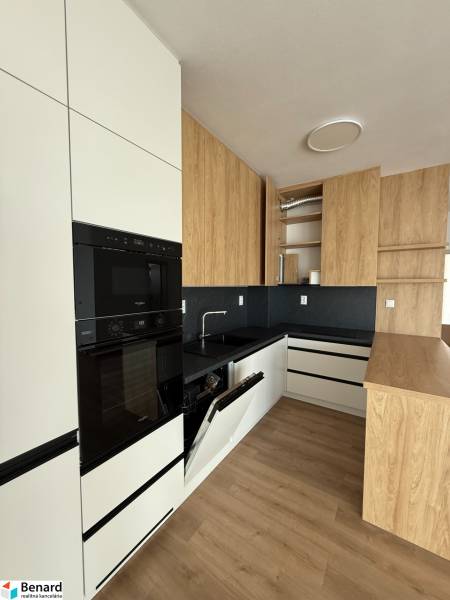 A modern kitchen with white cabinets and built-in appliances in a three-room apartment.