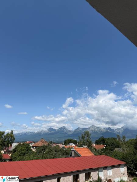 View from Hurbanova Street in Poprad towards the Tatras, with red roofs and a blue sky.