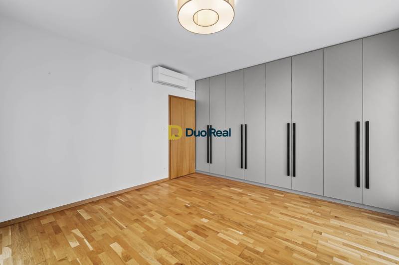 A spacious room with wooden flooring, a wardrobe, and air conditioning in a 3-bedroom apartment.