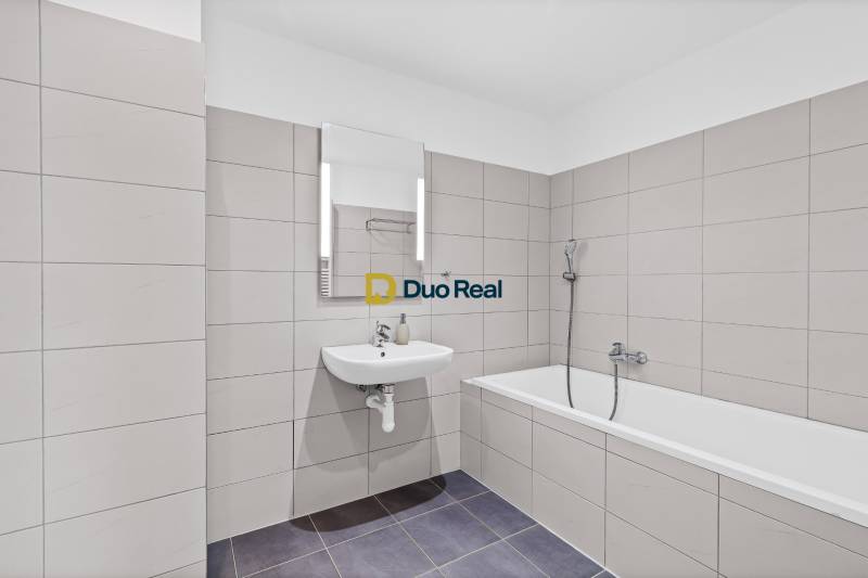A bathroom in a 3-room apartment with a bathtub and a sink, tiled with beige tiles.