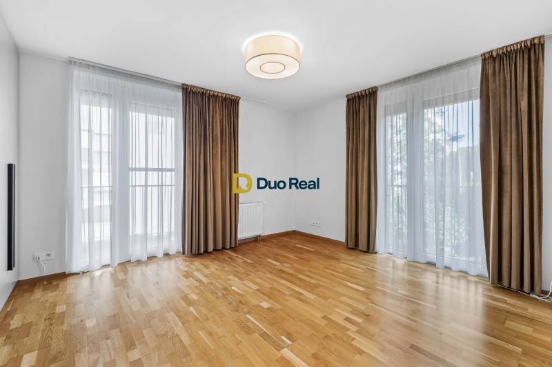 Spacious living room in a 3-room apartment with wooden flooring and large windows.