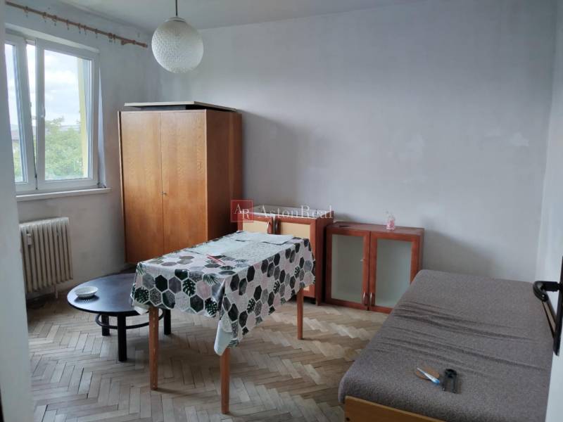 A room in a 2-room apartment with a wooden floor, a table, and a wardrobe.