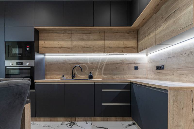 A kitchen unit with wooden paneling and black appliances in a 3-room apartment.