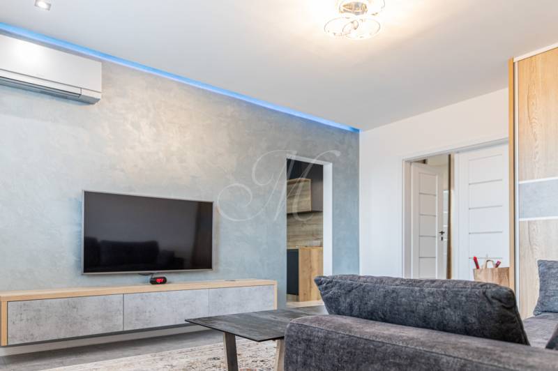 Living room in a three-room apartment with a gray sofa and a TV on the wall.