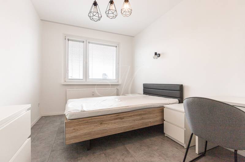 A bedroom with a gray bed and chair in a three-room apartment.
