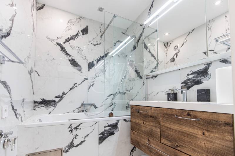 Bathroom with a glass shower, sink, and wooden storage in a 3-room apartment.