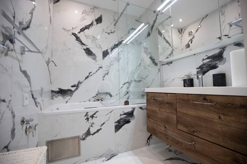 A bathroom with a marble wall, a bathtub, and a wooden cabinet in a 3-room apartment.