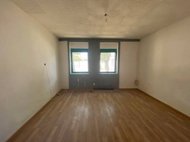 A room with a wooden floor and two windows as part of apartment construction.