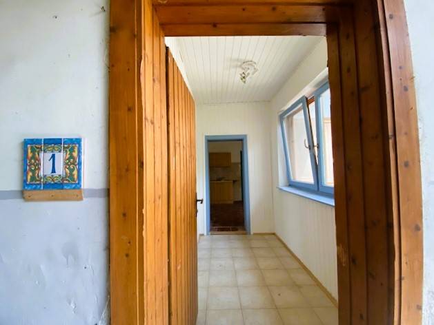 A room with a wooden door frame, tiles, and blue windows under apartment construction.