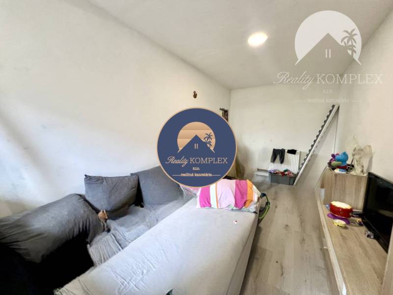 Living room with a sofa, television, shelf, and stairs in a family house.