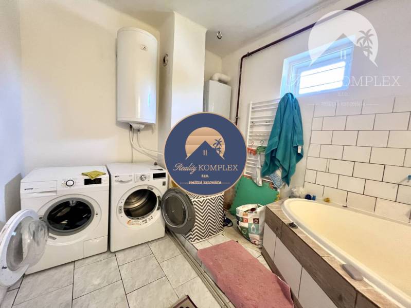 A bathroom in a family house with a washing machine, dryer, bathtub, and boiler.