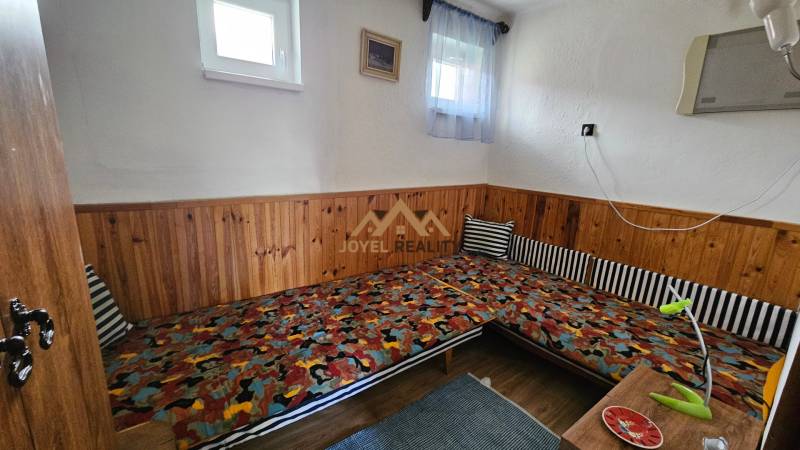 A room in a family house with wooden paneling, colorful mattresses, a small window, a lamp.