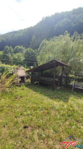 A garden gazebo and a fireplace by the cottage in Ružín, Malá Lodina, surrounded by wooded hills.