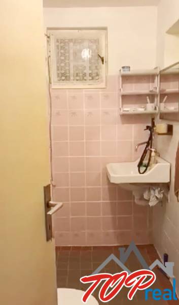 A bathroom in a cottage with pink tiles and a sink with a large faucet.