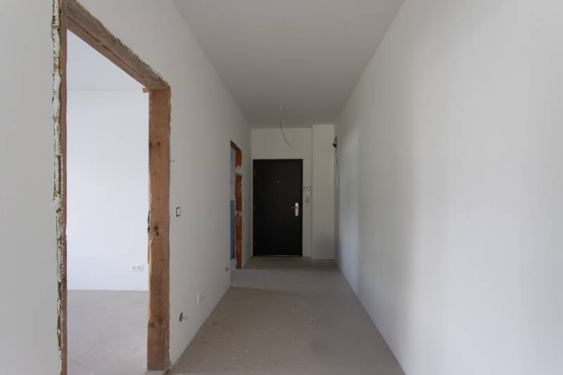 A hallway under construction in a 2-room apartment with white walls and black doors.