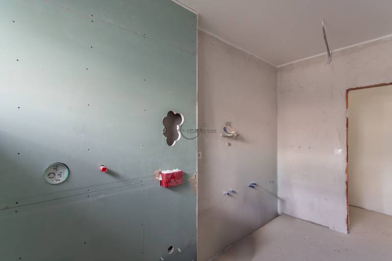 An empty room in a two-room apartment with prepared wiring and a drywall wall.