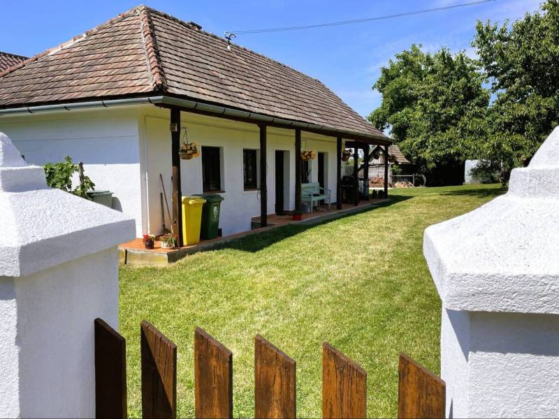 A family house in Pányok with a lawn, flowers on the terrace, a wooden fence, trees in the yard.