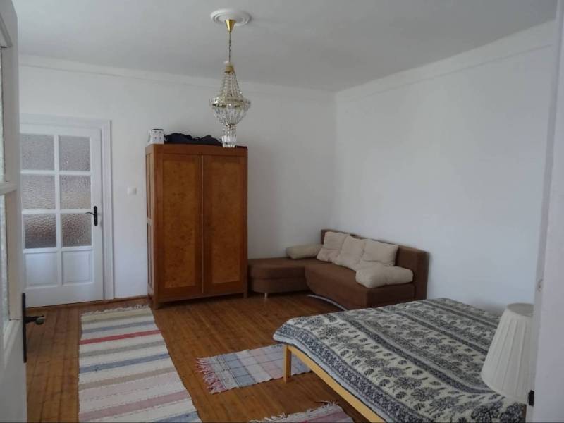 A room in a family house with a chandelier, a couch, a bed, and a wooden floor.