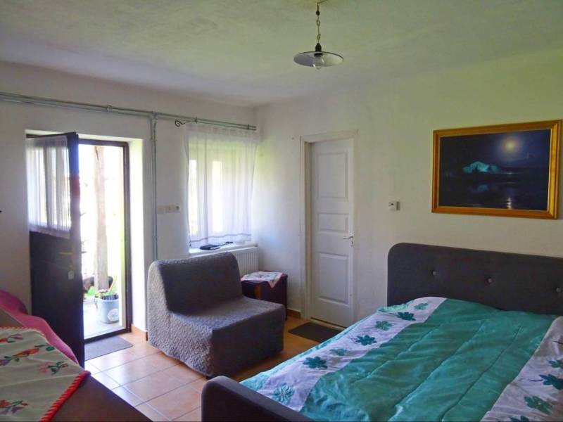 Interior of a family house with a bed, an armchair, and open doors to the terrace.