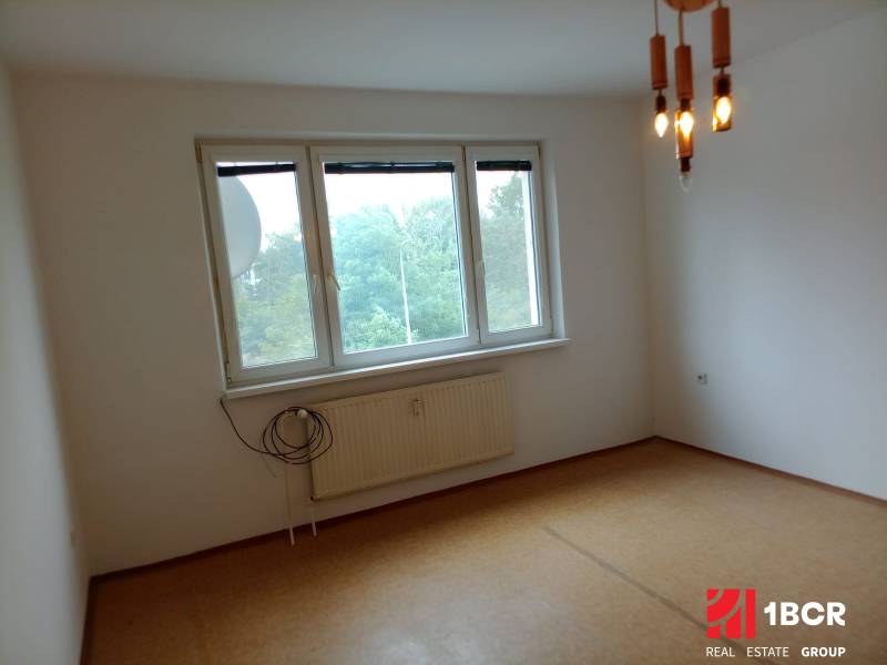 An empty room with a hanging light fixture and a window in a three-room apartment.