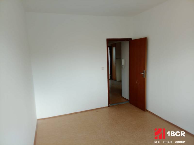 Empty room with a door in a 3-room apartment, parquet floor, white walls.
