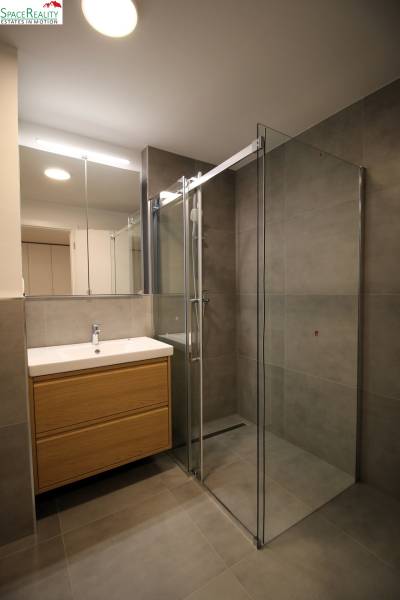 Bathroom with a shower and a sink with a wooden cabinet in a 2-room apartment.