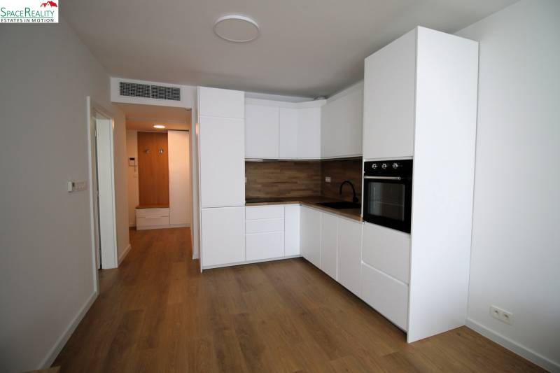 A kitchen in a 2-room apartment with white cabinets and wooden flooring.