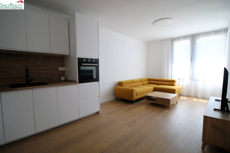 Living room in a two-room apartment with a white kitchen and a yellow sofa, bright environment.
