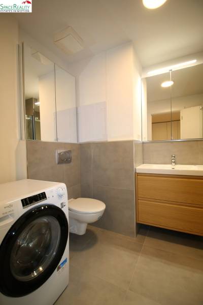 A bathroom in a 2-room apartment with a washing machine, toilet, and wooden washbasin counter.