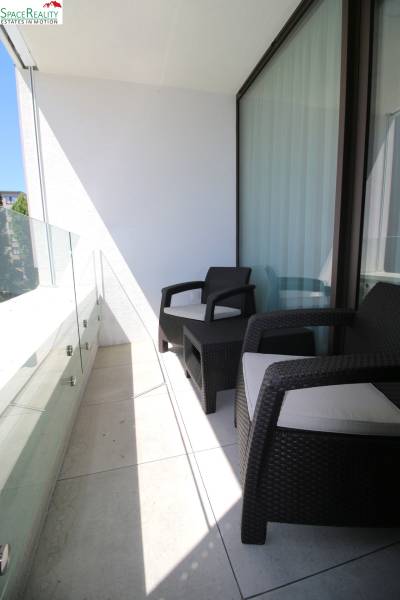 A balcony with two chairs and glass railing in a 2-room apartment.