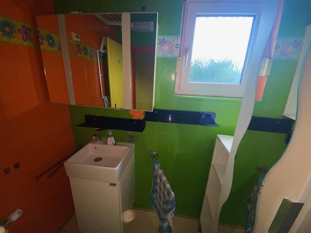 A colorful bathroom in a family house with a sink and a mirror.