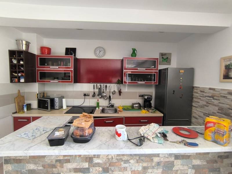 A kitchen in a 2-room apartment with furnishings, red cabinets, and a marble countertop.
