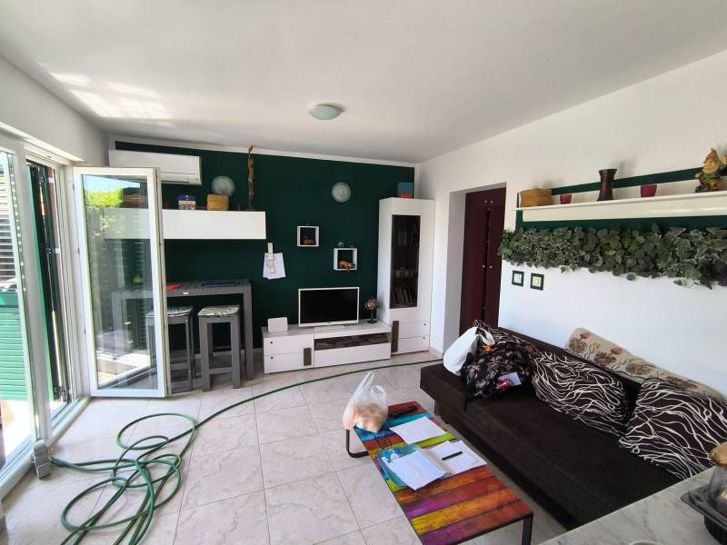 Living room in a two-room apartment with a dark sofa, decorations, and open glass doors.