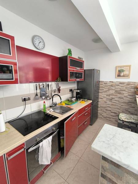 Kitchen in a 2-room apartment with red cabinets, a cooktop, and a stainless steel refrigerator.