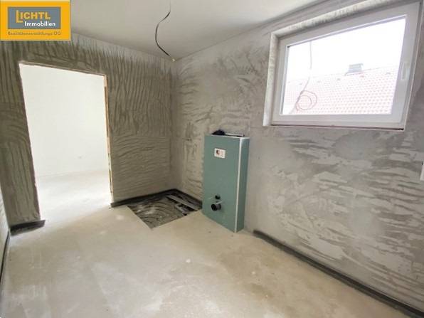 A room under construction with a window, the floor is concrete, the room will be in a 5 or more room apartment.
