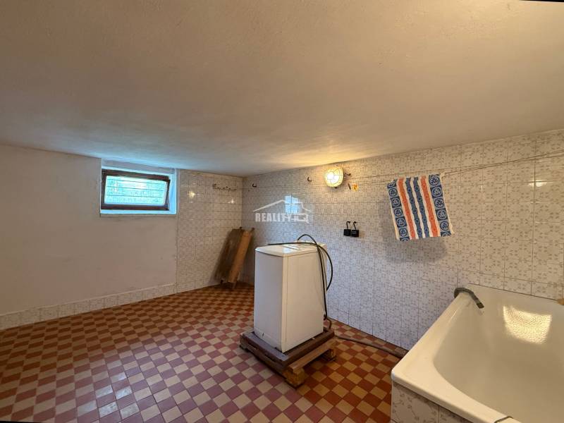 Laundry room in a family house with a bathtub, washing machine, and window.