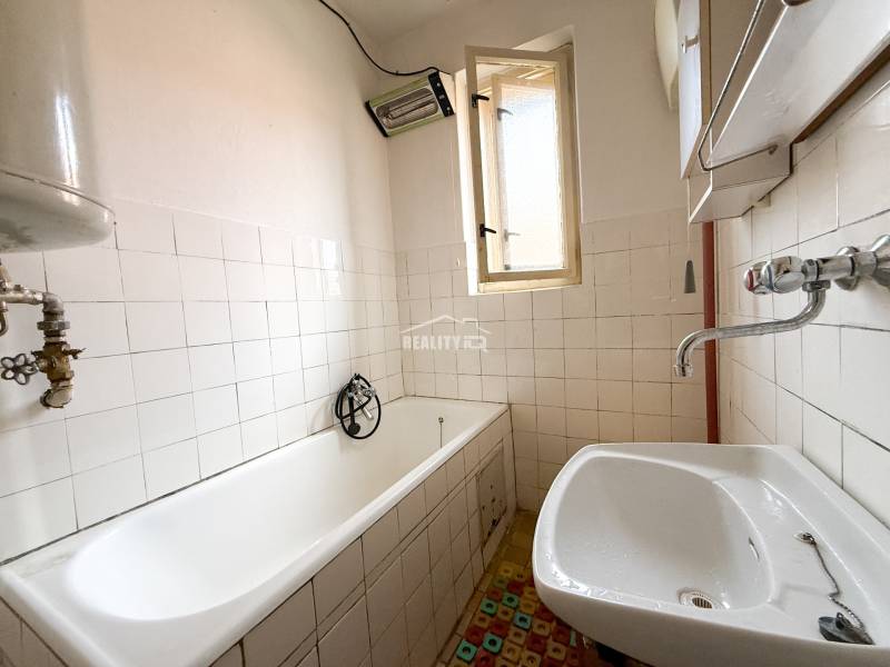 A bathroom in a family house with an older bathtub, a sink, and a window.